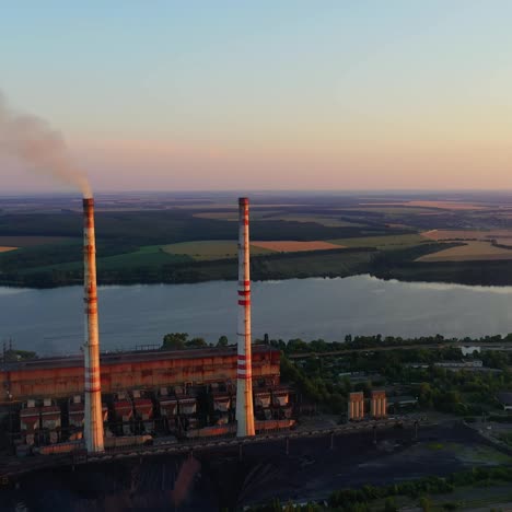 chemical plant among beautiful nature. industrial factory with smoking pipe near the river at sunset. pipe emits harmful emissions and pollute the environment. aerial view.