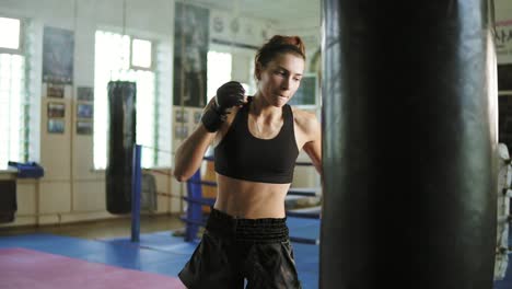 close up view of caucasian female kickboxer hitting the punching bag with her hands and legs in the gym alone. tough power