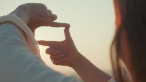 close up rear view of woman framing sun with hands, soft golden light filtering through fingers creating lens flare and dreamy blurred backdrop evoking