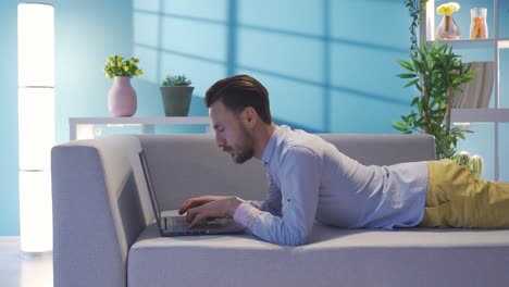 elegante hombre de negocios acostado en el sofá en casa usando una computadora portátil, descansando y haciendo su trabajo.