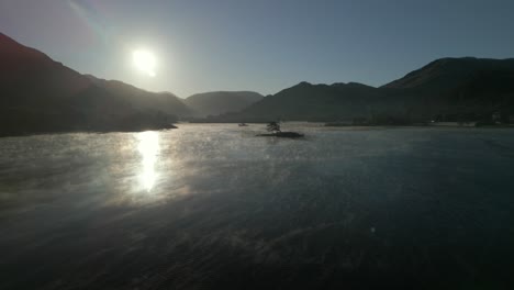 Sunrise-reflected-in-calm-misty-lake-with-flight-towards-silhouetted-small-island