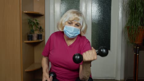 elderly senior grandmother making weight lifting dumbbells exercising during coronavirus lockdown