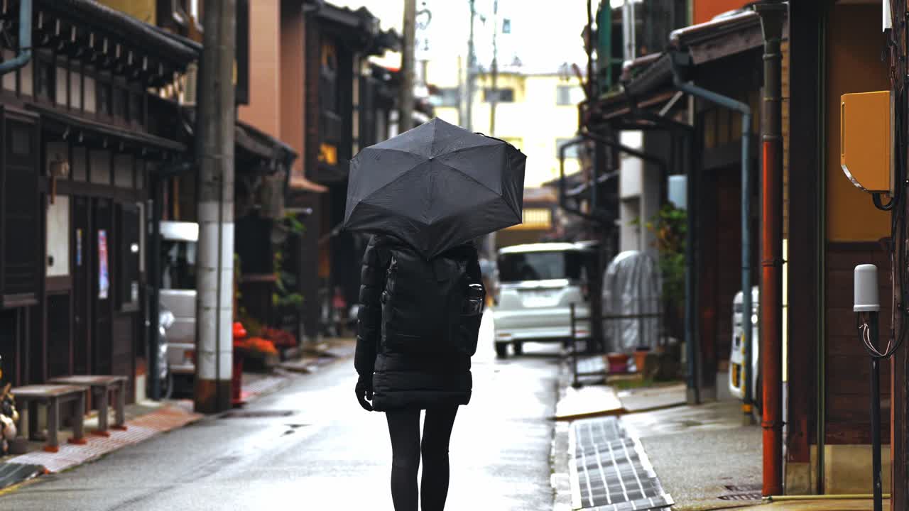 A woman strolls through the charming streets of Takayama’s historic district, holding an umbrella as rain gently falls.
