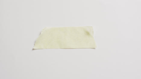 Video-of-close-up-of-torn-piece-of-yellow-paper-on-white-background