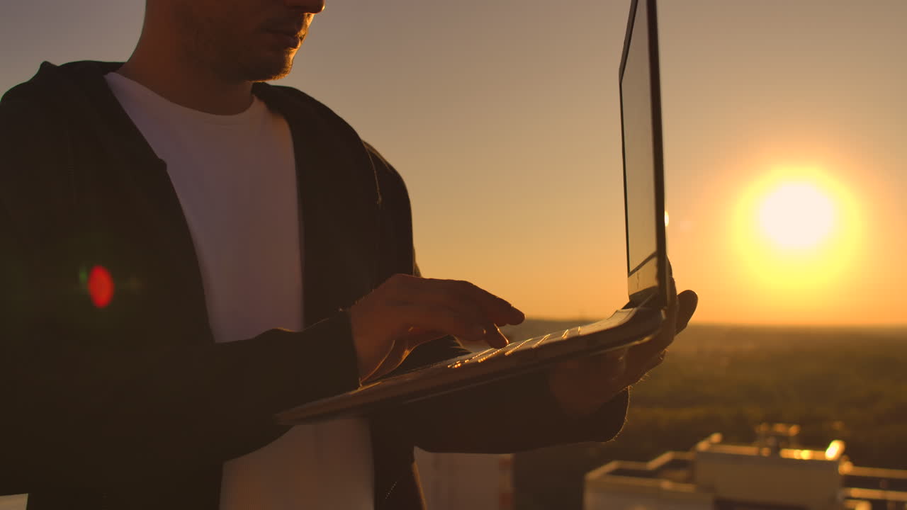 primer plano: la mano de un programador escribiendo en un teclado de portátil al atardecer con vistas al techo. un hombre de negocios trabaja remotamente. freelance realiza trabajo en vacaciones