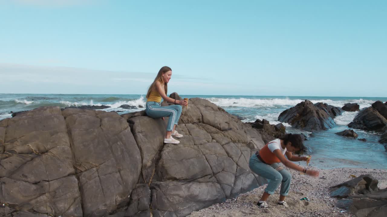 vista lateral de un caucásico y una chica de raza mixta comiendo helado en la playa