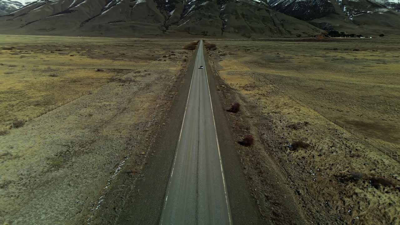 disparo aéreo que muestra un coche en la carretera en patagonia con cadenas montañosas y picos nevados en el fondo, argentina