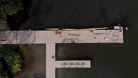 vista aérea constante de arriba hacia abajo de un embarcadero de remo y un centro de entrenamiento en el lago de la ciudad de río de janeiro con remeros que llegan y salen del agua llevando los botes al almacenamiento fuera del marco