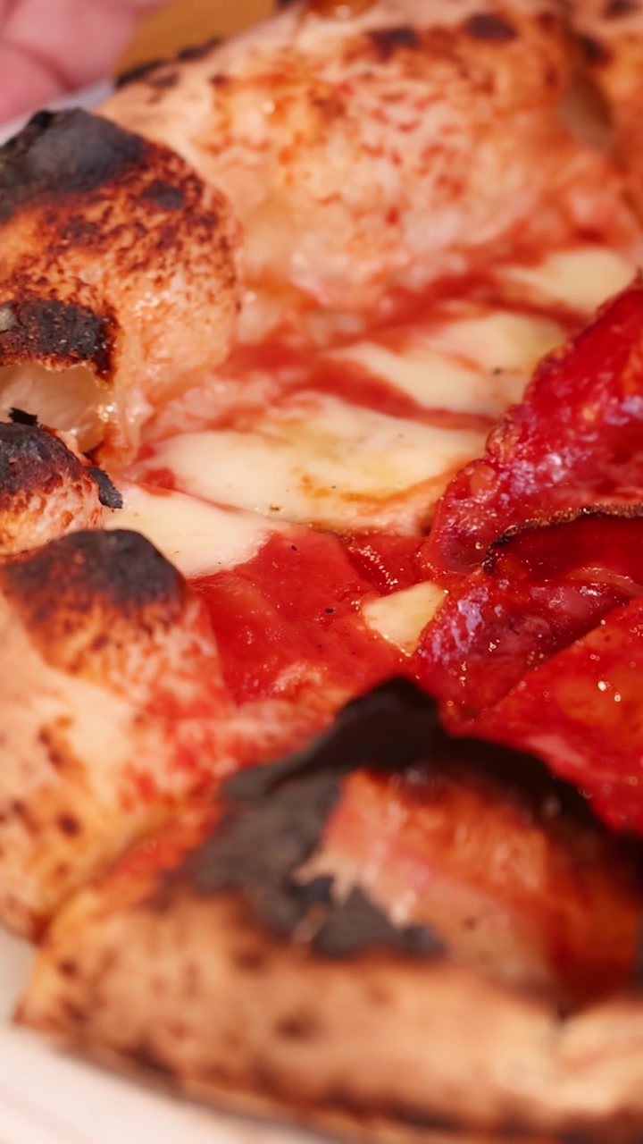 Scatto macro di pizza ai peperoni con bordo carbonizzato e formaggio fuso su piatto bianco.