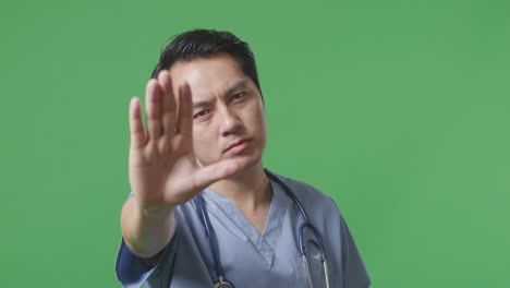 close up of asian male doctor with stethoscope making stop gesture while standing on green screen background in the hospital