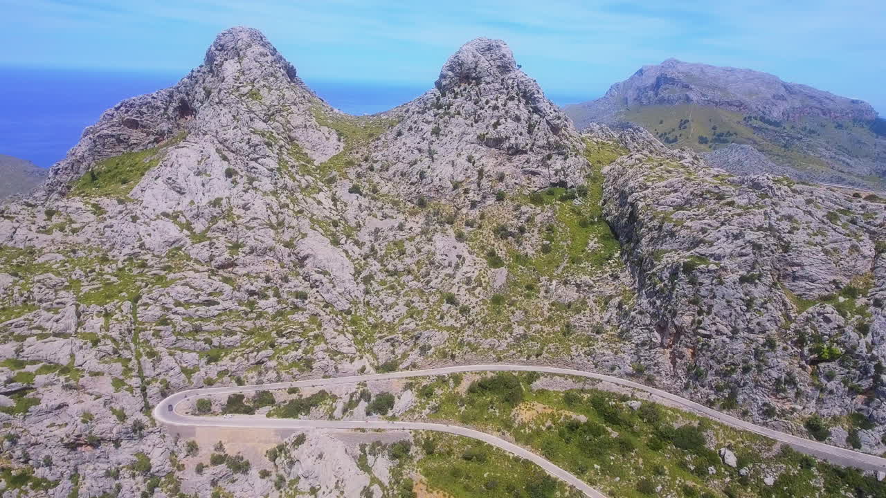 Højtliggende luftfoto af en snoet bjergvej med en bus og bil, bjerge og hav synlige i det fjerne på Mallorca