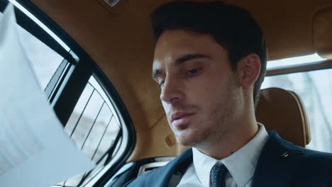 Portrait-of-focused-male-professional-checking-data-in-paperwork-in-modern-car.