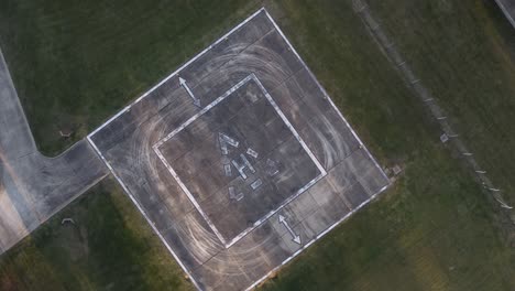 Aerial-top-down-shot-of-empty-heliport-or-helipad-on-field-during-daytime---orbit-and-landing