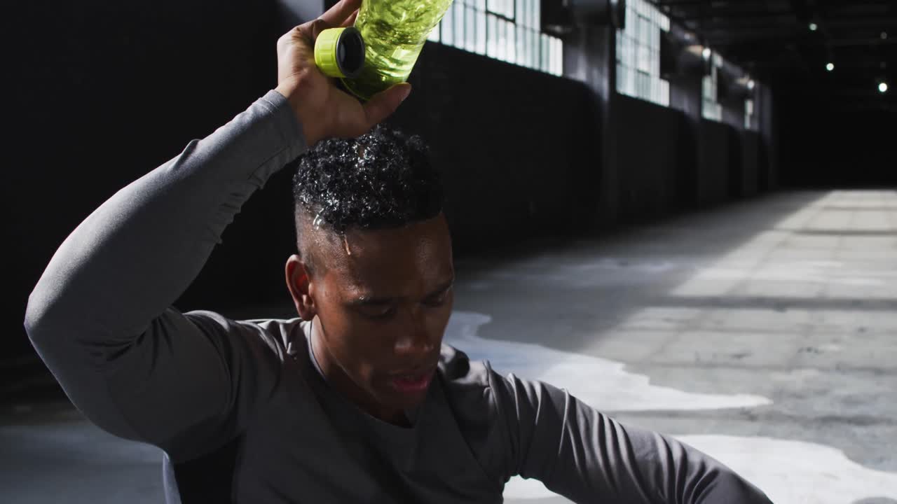 African american man sitting in an empty building pouring water on his head