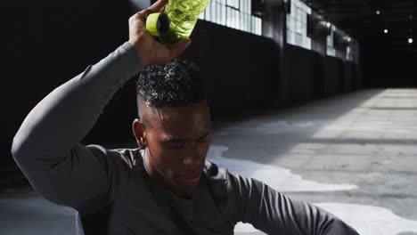 African-american-man-sitting-in-an-empty-building-pouring-water-on-his-head