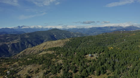 aerial moving over small mountain cabin with snow covered peaks in distance, 4k