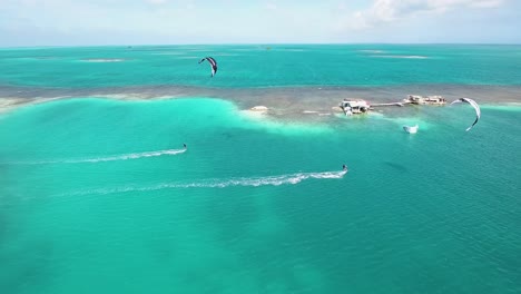 Aerial-View-Two-Men-Kitesurf-In-Paradise,-Palafito-Los-Roques-Archipelago