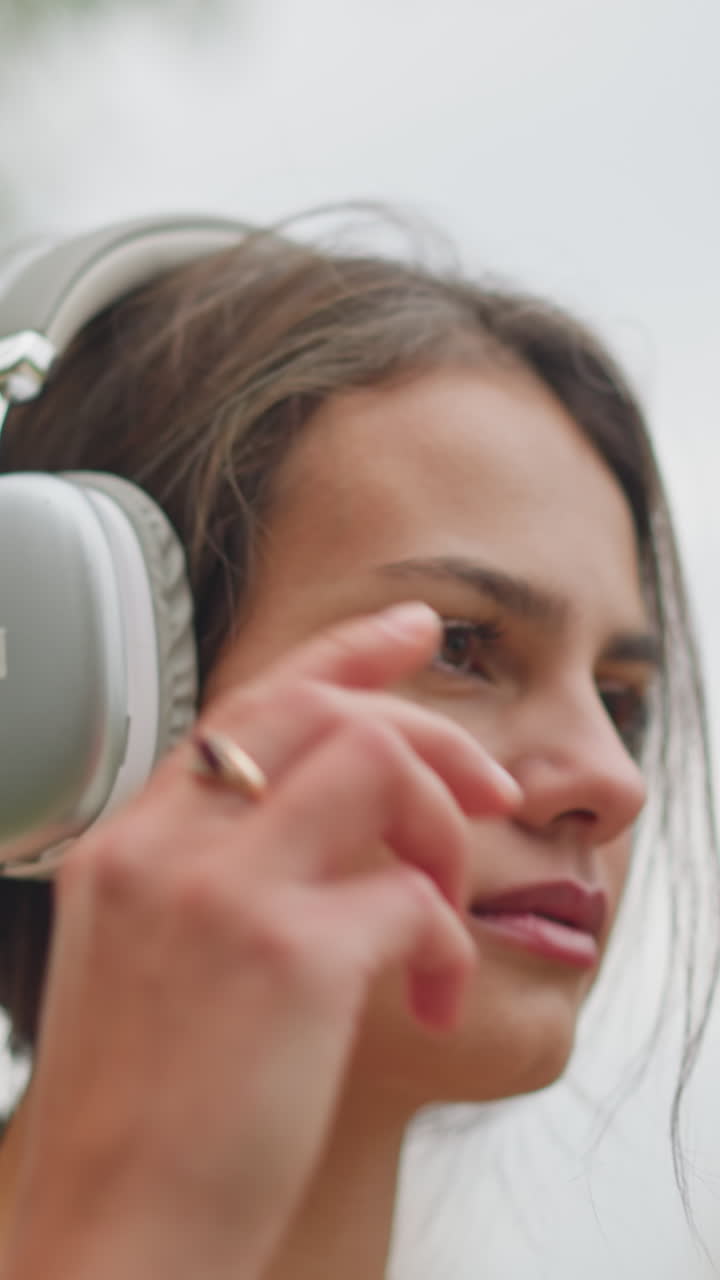 Close-up view of beautiful young lady wearing headphones on her head outdoors, with a calm and focused expression, enjoying her time with music, highlighting her natural beauty