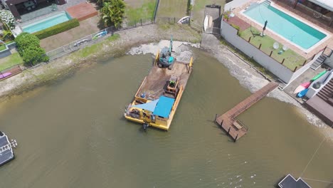 drone footage captures a barge with construction equipment working on a canal near luxury homes in broadbeach waters