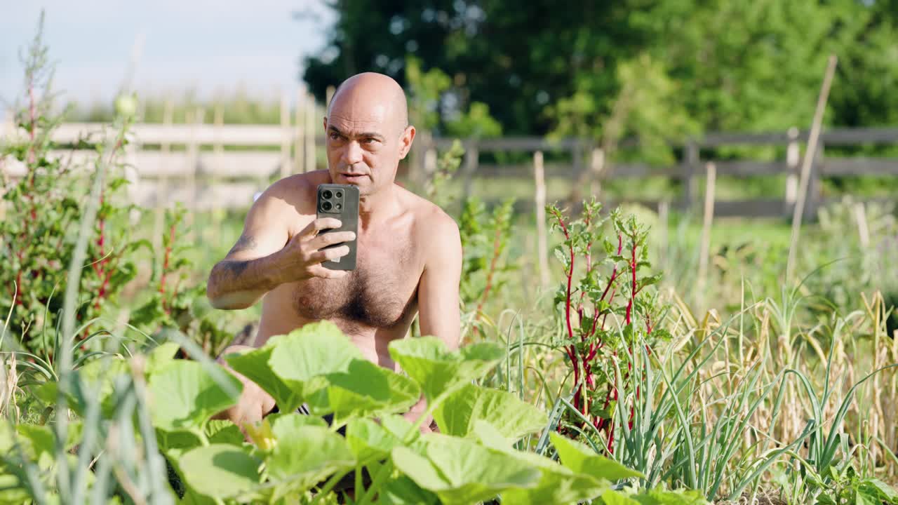 Shirtless gardener recording a video selfie in a vegetable garden