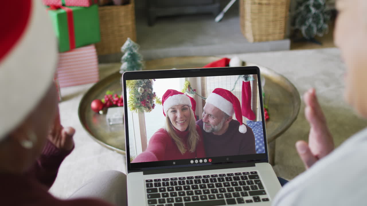 diversas amigas mayores que usan una computadora portátil para una videollamada de navidad con una pareja en la pantalla