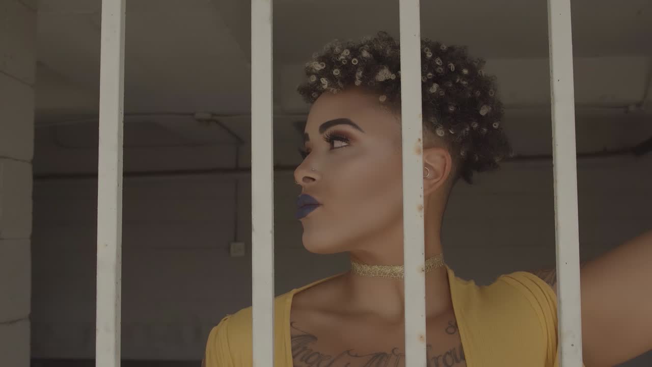 A woman with dark blue lips and a yellow dress dancing behind the metal grill