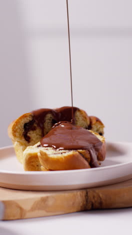 vertikale nahaufnahme von geschmolzener schokoladensauce, die auf schokoladen-babka-brötchen auf teller 2 gegossen wird