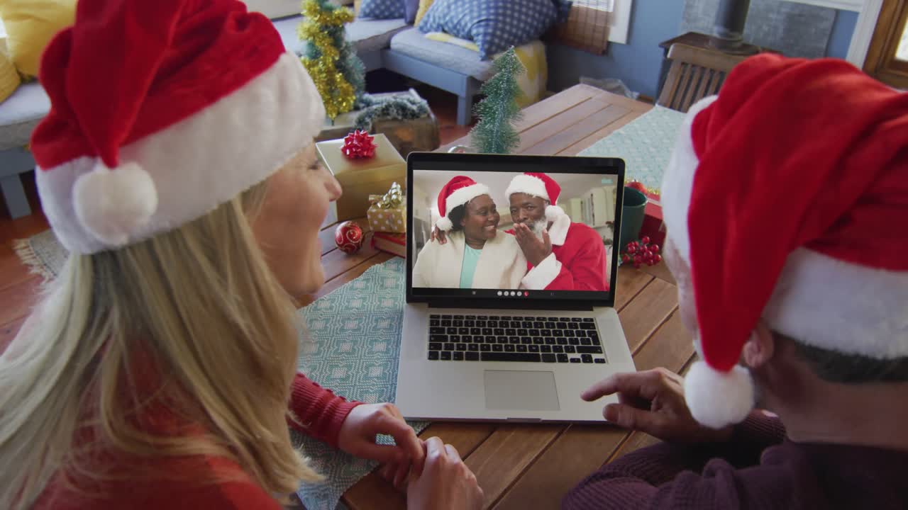 pareja caucásica con sombreros de santa usando una computadora portátil para una videollamada de navidad con la pareja en la pantalla