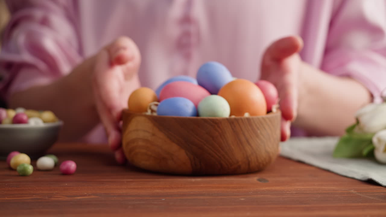 Person Placing Colorful Easter Eggs in Wooden Bowl on Table