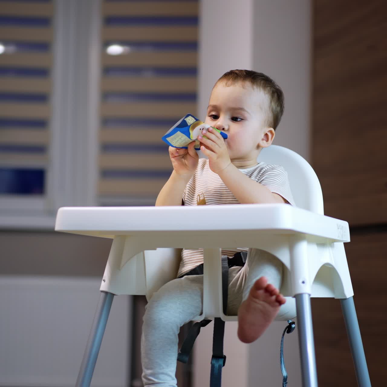 Relaxed little kid eating fruit puree from plastic tube. Sweet kid enjoying baby food from pack. Low angle view