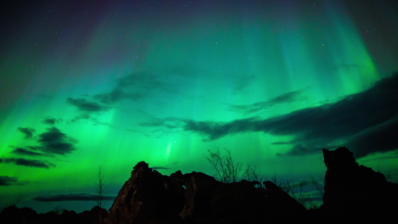Aurora borealis som lyser med grønne og blå søyler med skyer over lavafelt, nordøst på Island. Tidsforløp
