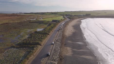 coastal road, winter sun and few walker on a sandy beach with foaming waves in slow motion