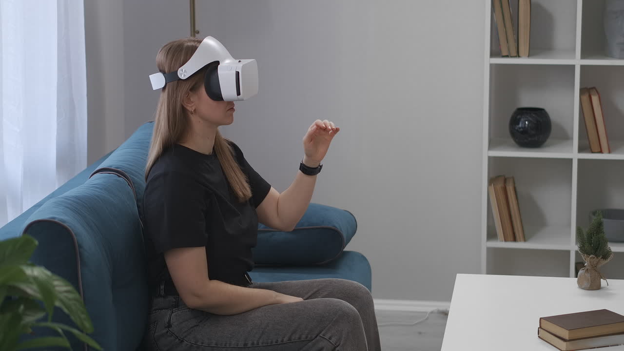 mujer jugador está usando hmd-display sentado en el sofá en la sala de estar tecnología moderna de la realidad virtual mujer está gesticulando con las manos dispositivo del futuro