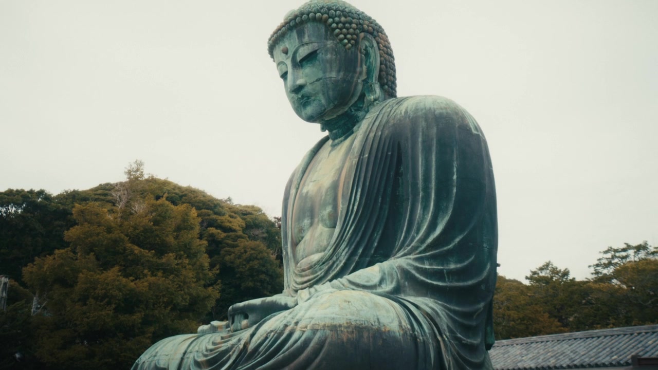 Vista drammatica dal basso del Grande Buddha (Daibutsu) di Kamakura presso il tempio Kotoku-in, che evidenzia la scala imponente della statua e la patina bronzo-verde invecchiata.