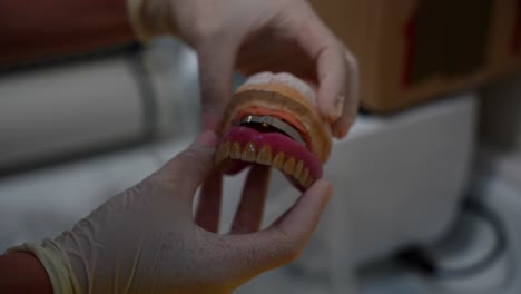 Manos-De-Higienista-Con-Guantes-Que-Muestran-Las-Partes-Superior-E-Inferior-De-Una-Dentadura-Postiza