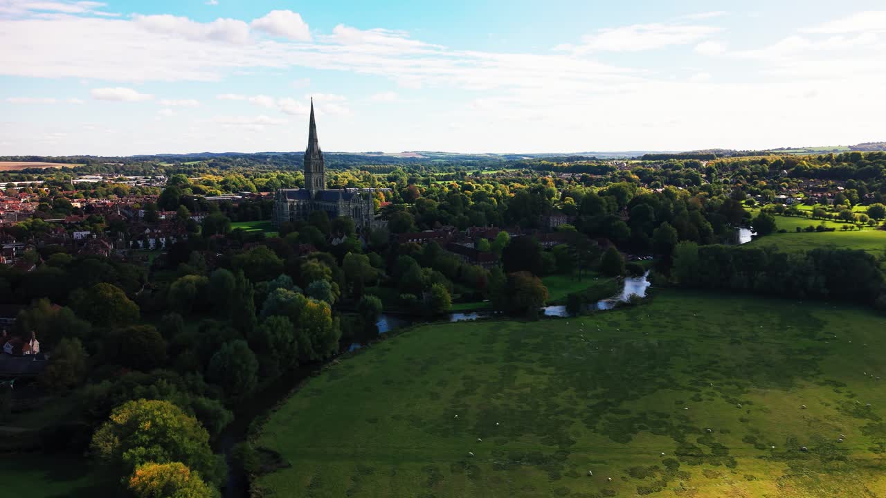 Lotniczy widok z drona na Katedrę w Salisbury otoczoną rzeką Avon i zieloną okolicą w Wiltshire, Anglia. Malowniczy krajobraz historycznego miasta katedralnego z drzewami, polami i tradycyjną angielską zabudową.
