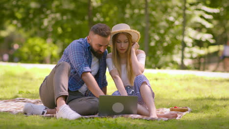 una pareja usando una computadora portátil en un picnic en el parque