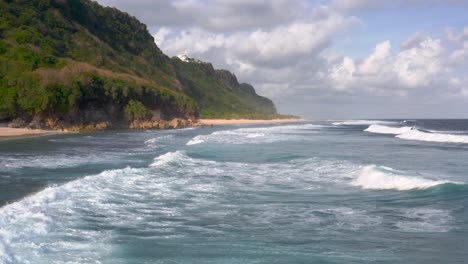 Aerial-view-of-low-tides-moving-towards-the-shore-of-beach-surrounded-by-huge-green-cliffs