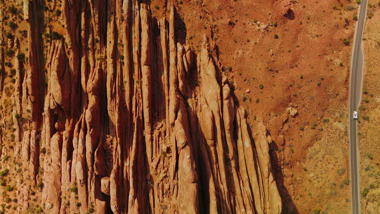 Road going parallel to the beautiful rocks in Arches National Park. Drone flying over the orange landscape in Utah, USA.