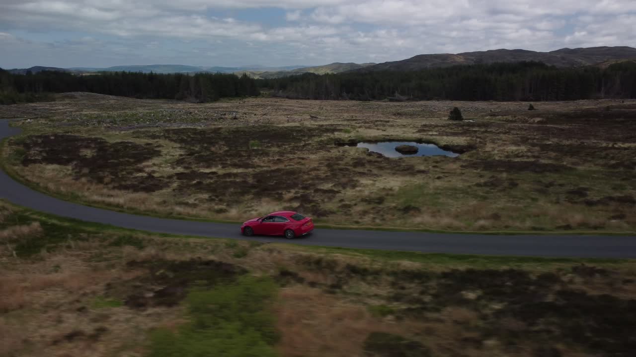 Ripresa in movimento di un'auto rossa che viaggia lungo una strada di campagna a corsia unica.