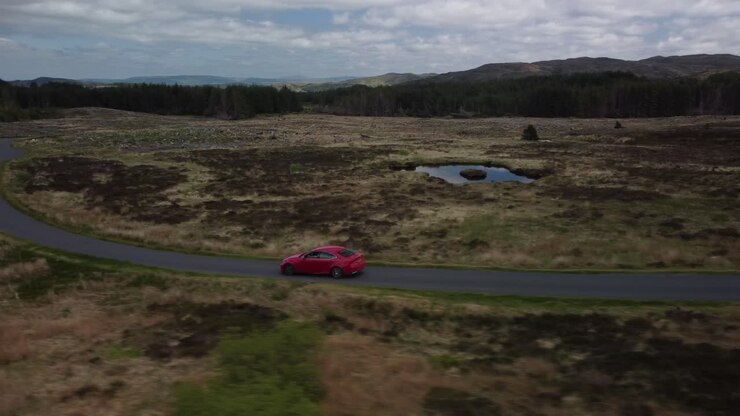 Ripresa in movimento di un'auto rossa che viaggia lungo una strada di campagna a corsia unica.