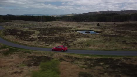 disparo de seguimiento de un coche rojo que viaja a lo largo de una carretera de campo de una sola pista