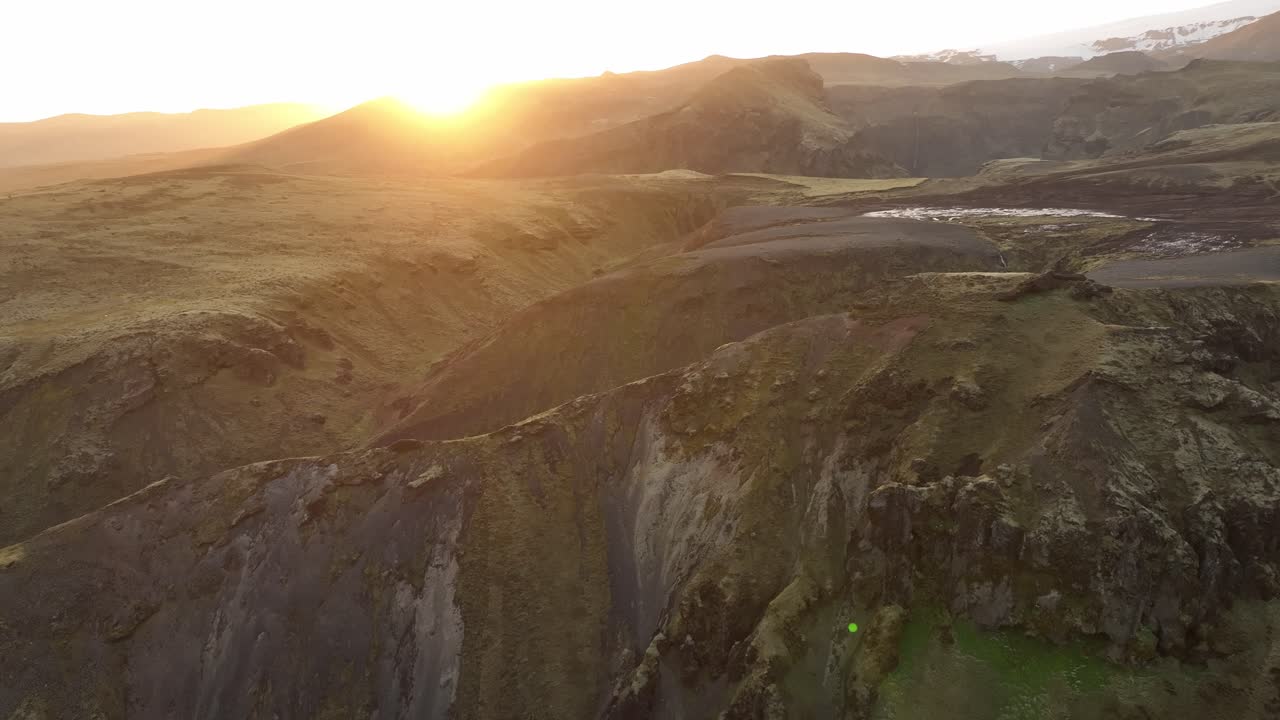 Aerial view of sunrise over volcanic ridges in northern Iceland, casting warm light across the rugged, untouched highland landscape.