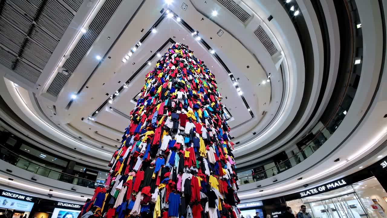 A low-angle shot of a vibrant, towering art installation made of colorful clothes in a modern mall
