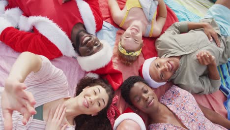 six diverse happy friends celebrating christmas in costumes, lying outdoors waving to camera