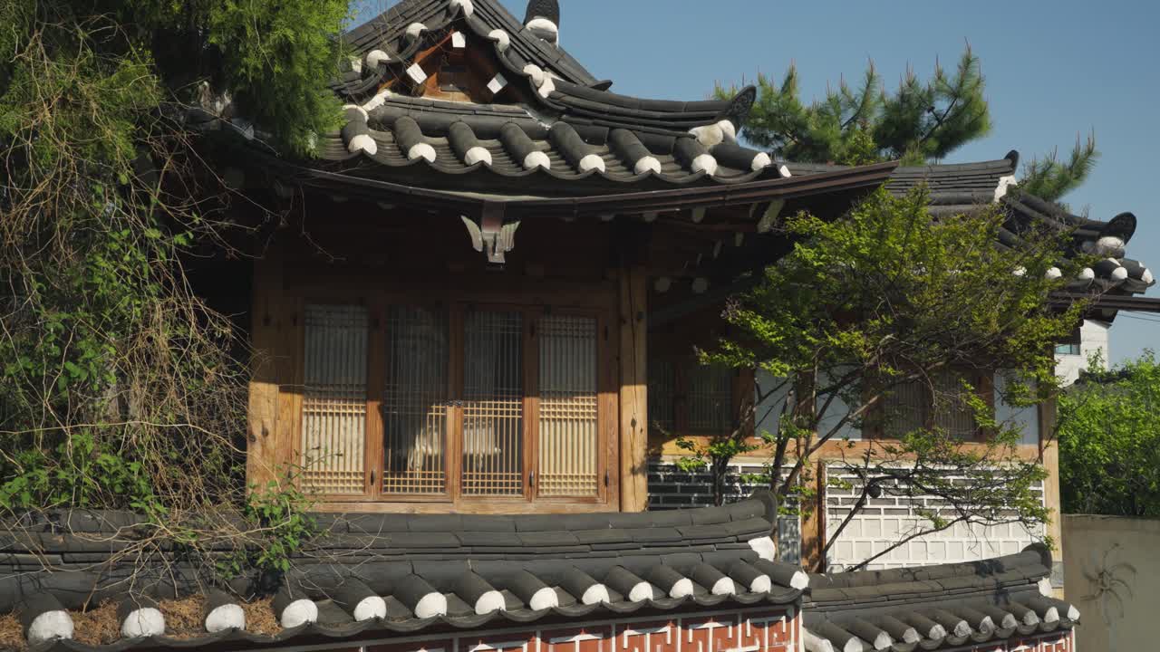 A view slowly moves closer to a traditional Korean Hanok building, highlighting its ornate roof tiles, wooden window frames, and surrounding lush greenery, Dolly Push In