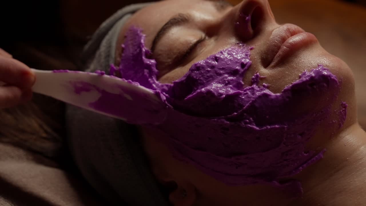 Donna che riceve un trattamento viso con maschera viola in una spa