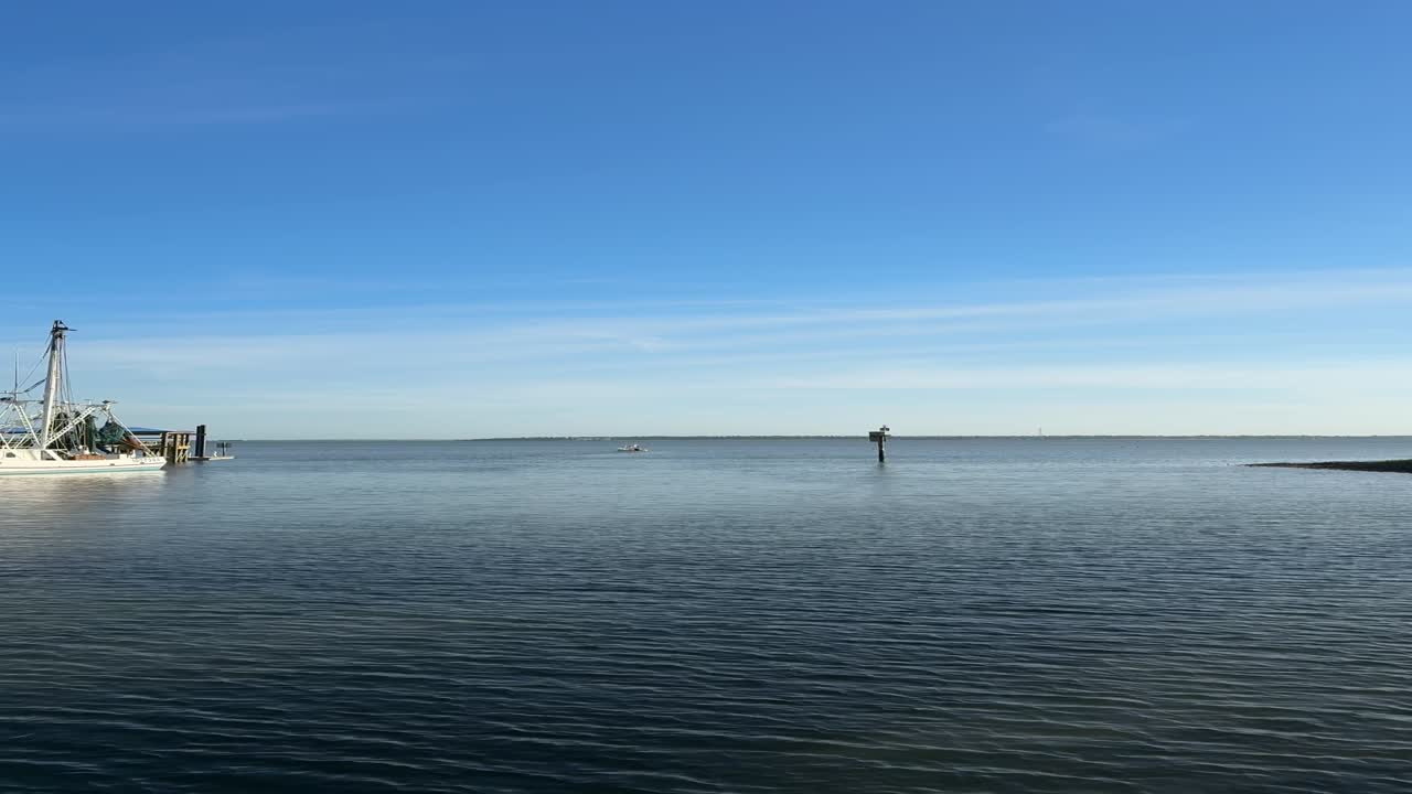 Eine vertikale Aufnahme mit hoher Bildrate (60fps) eines weißen kommerziellen Fischerboots, das am Shem Creek in Mount Pleasant, South Carolina, angedockt ist. Das Filmmaterial zeigt sanfte Wasserbewegungen und Vögel im Flug