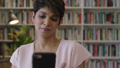 retrato de una hermosa y elegante mujer hispana enviando mensajes de texto navegando utilizando la tecnología de aplicaciones móviles de teléfonos inteligentes en el fondo de la estantería de la biblioteca