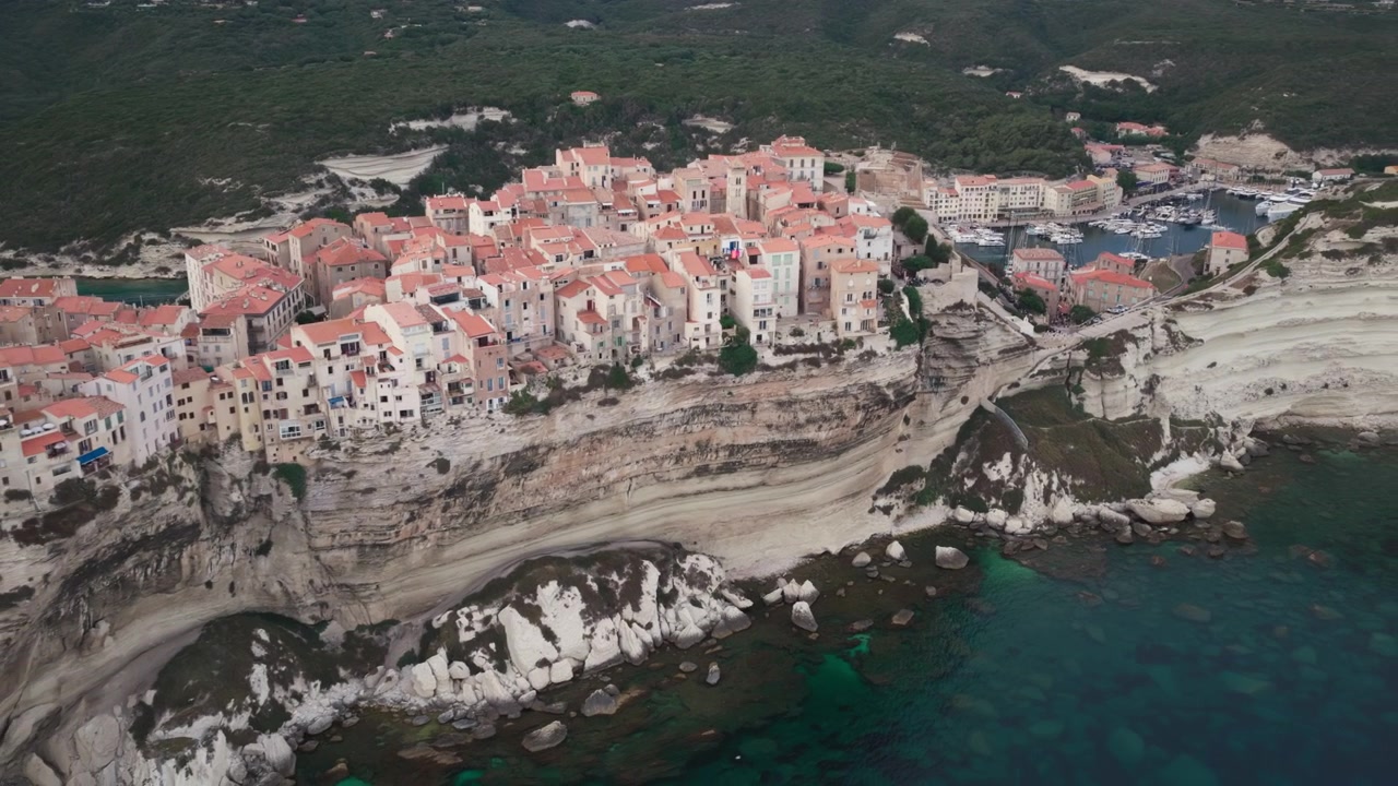 Una veduta aerea al tramonto sulle scogliere calcaree e gli edifici storici del centro storico di Bonifacio in Corsica, Francia, con yacht di lusso nel porto protetto e l'acqua turchese del Mediterraneo.